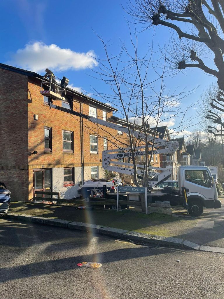 Cherry picker in use on Sunderland Road, Forest Hill, SE23, providing high-level access for roof maintenance. Two workers are on the elevated platform, and the cherry picker is securely positioned with stabilizers.